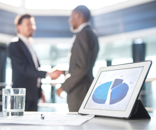 Two people in business suits shake hands in the background, while a tablet displaying a blue pie chart—highlighting payroll pros and cons—sits on a table in the foreground next to a glass of water and a pen.