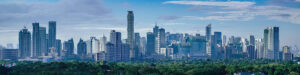 Wide-angle view of a modern city skyline with many tall skyscrapers under a partly cloudy blue sky, dense green trees in the foreground—an inspiring scene reflecting the growth of Philippine outsourcing in our 2026 Outsourcing Guide.