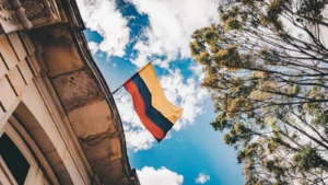 A Colombian flag waves from a building against a blue sky with clouds and tall trees in the background, reflecting Colombia’s vibrant spirit—a top destination for nearshore outsourcing and its many benefits.