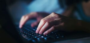 A close-up of hands typing on a laptop keyboard in dim lighting, with the keys softly illuminated by the screen’s glow—highlighting essential data entry skills in action.