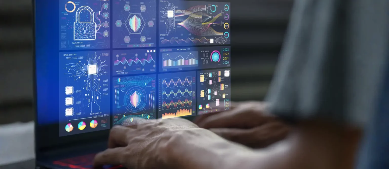 A person types on a laptop displaying multiple futuristic digital graphs, charts, padlock icons, and cybersecurity data visualizations on a transparent screen interface.