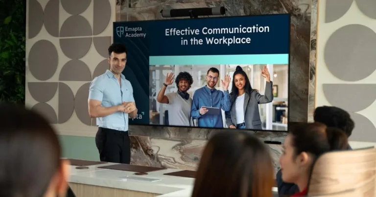A man stands in front of a group, presenting a slide titled Effective Communication in the Workplace for an AI-ready workforce, with an image of four smiling people waving on the screen.