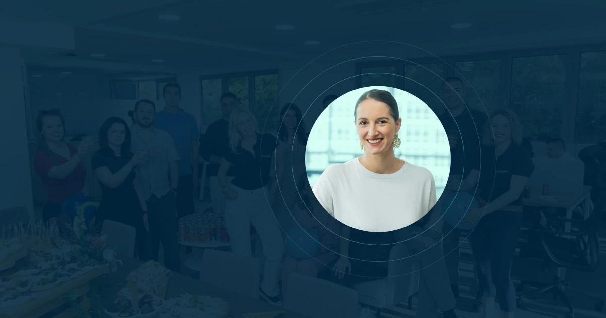 A group of people posing and smiling in an office, with a circular cutout highlighting a woman in a white top, smiling at the camera, centered in the foreground—perfect for discussing B Corp Certification on a podcast.